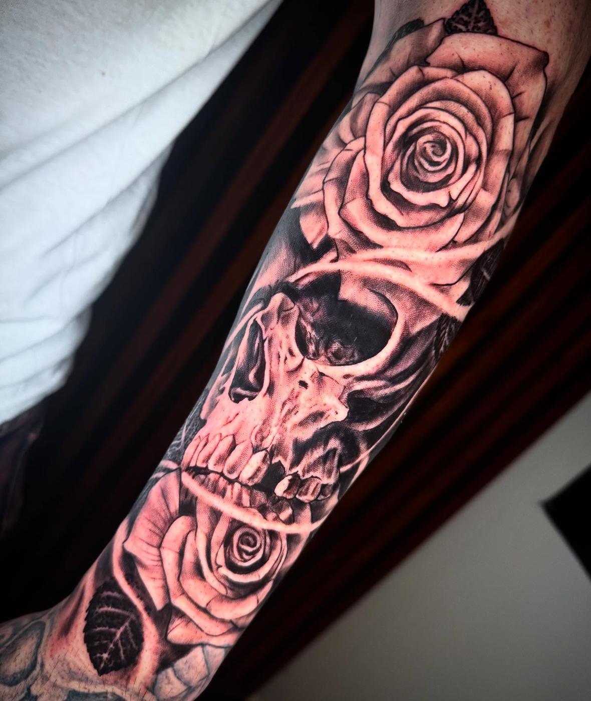 A black and gray skull between two roses, running down a forearm.