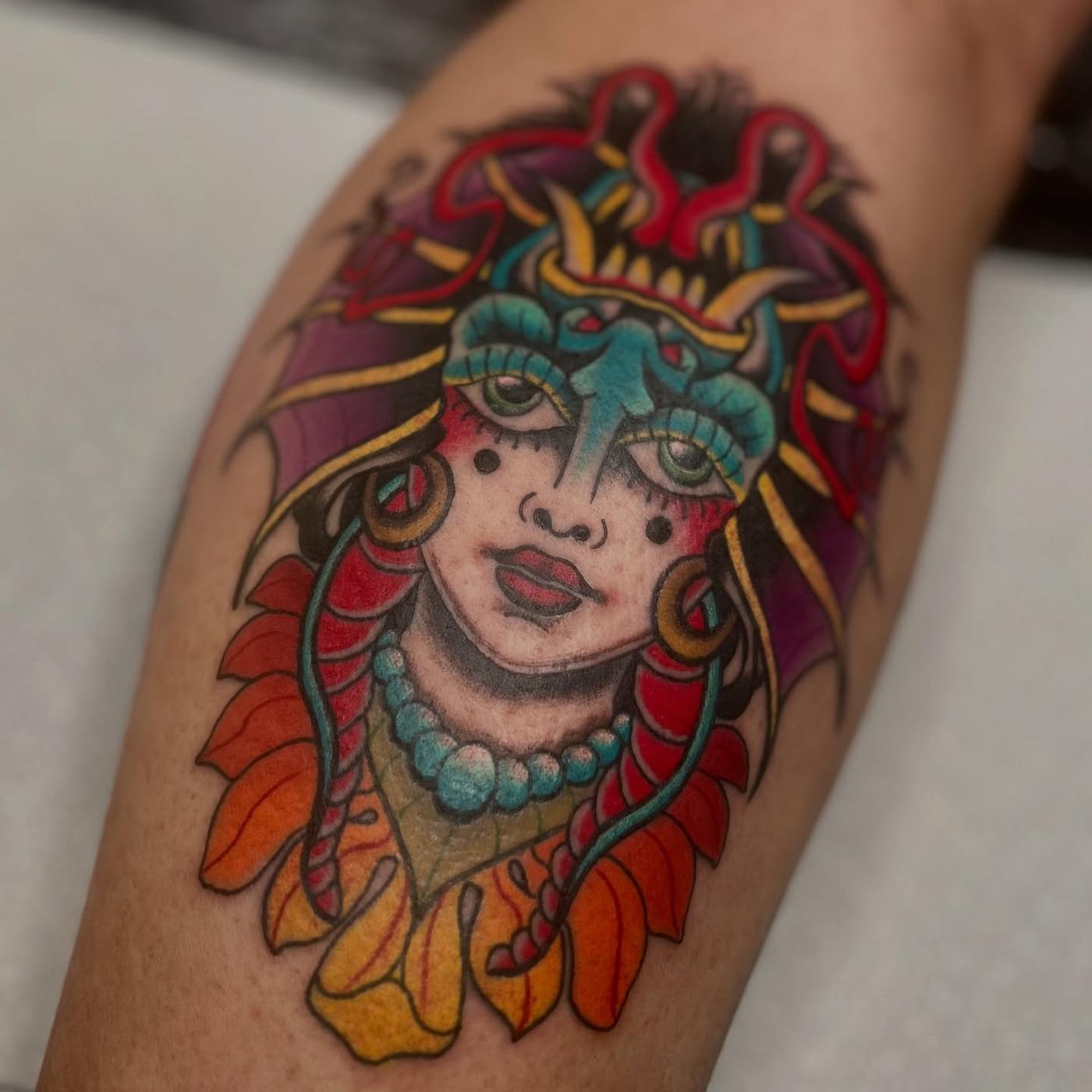 A neo-traditional portrait of a woman in a horned mask and feathered headdress, in vivid color, on a calf.