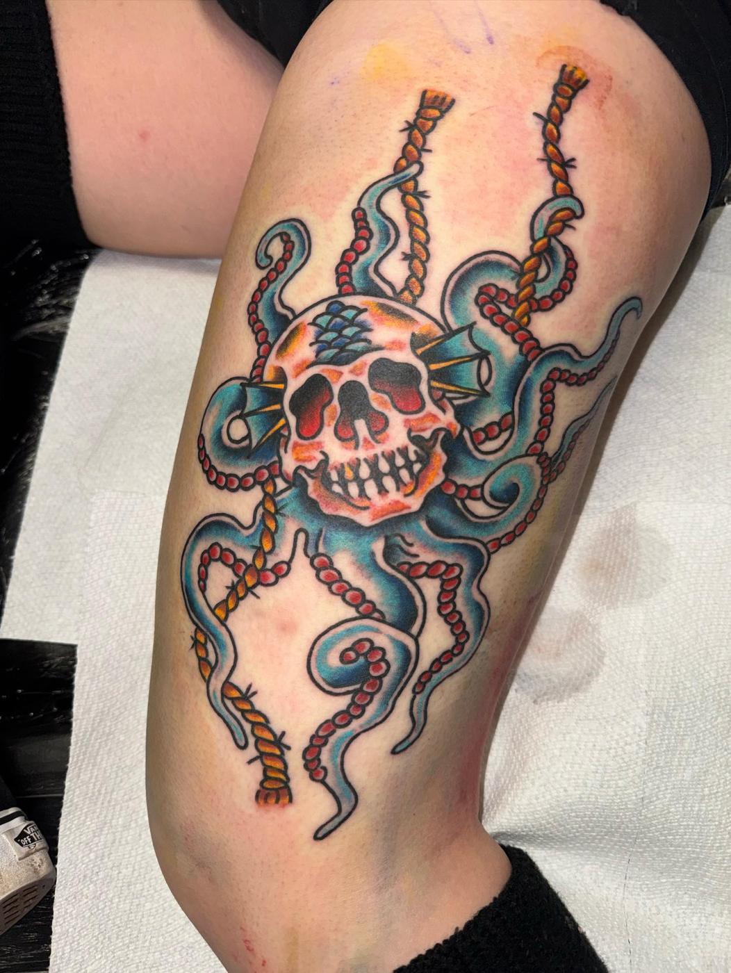 A traditional skull wrapped in octopus tentacles and rope, in blue and red, on a thigh.