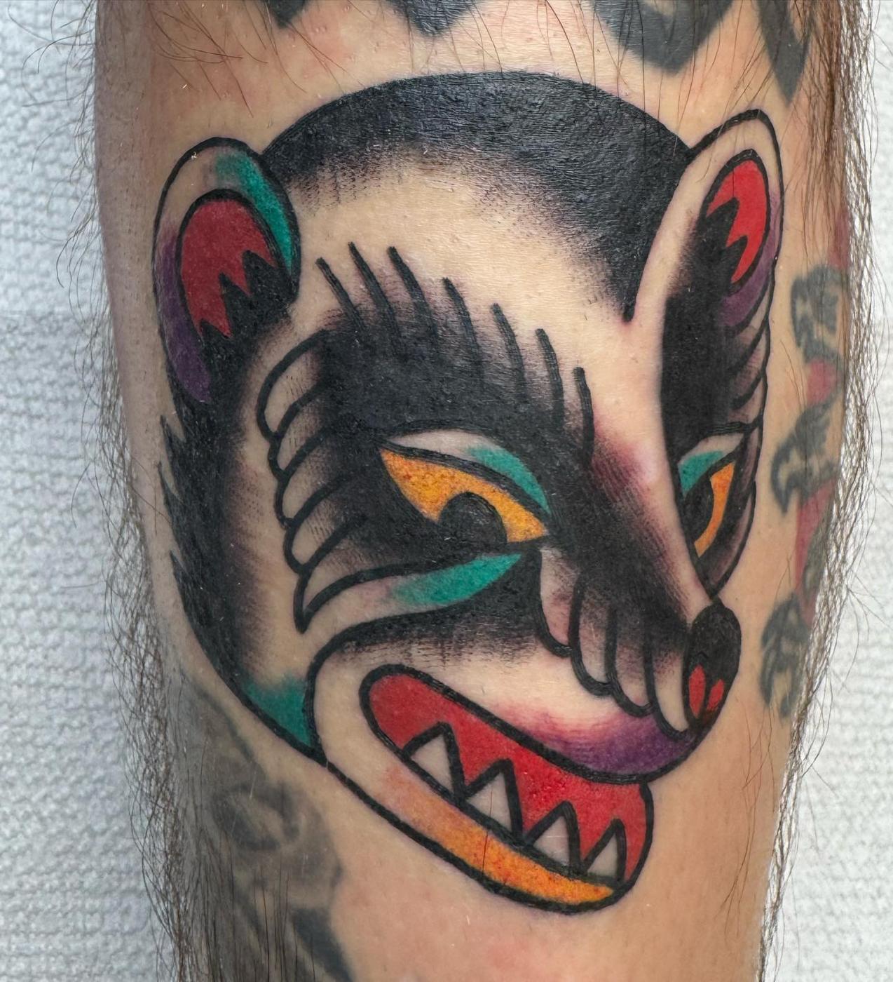 A traditional grinning fox head in black, red and teal, on a calf.