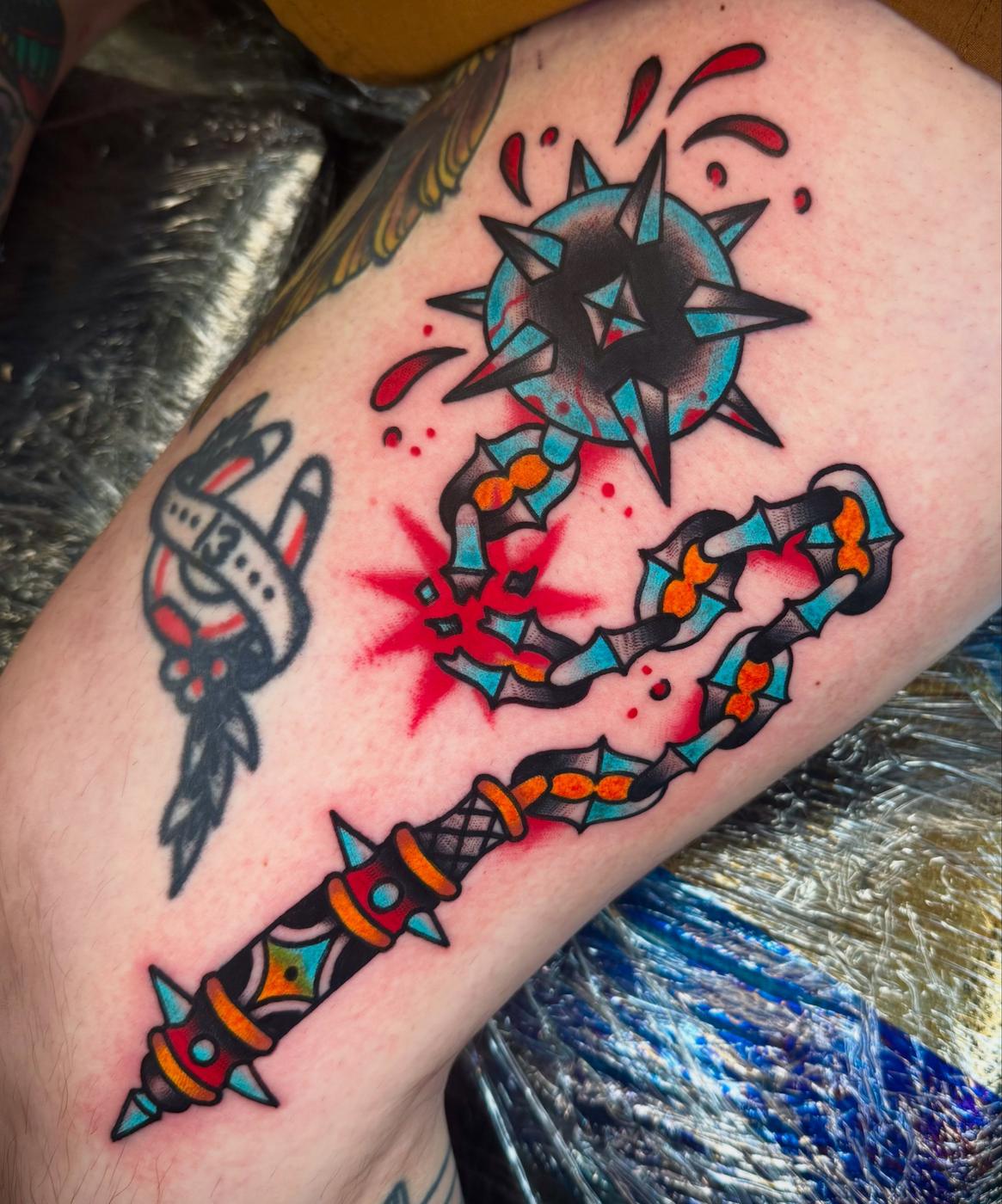 Traditional spiked flail in teal, orange and red on a thigh.