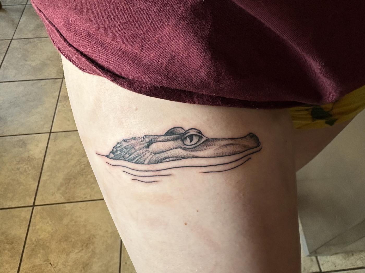 Small fine-line alligator surfacing through water lines, on a thigh.