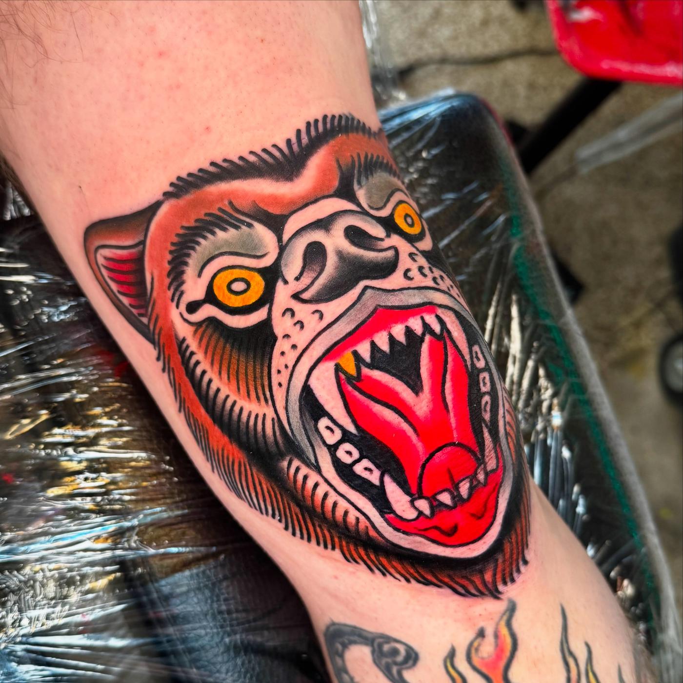 Traditional gorilla head in red and orange on a forearm.