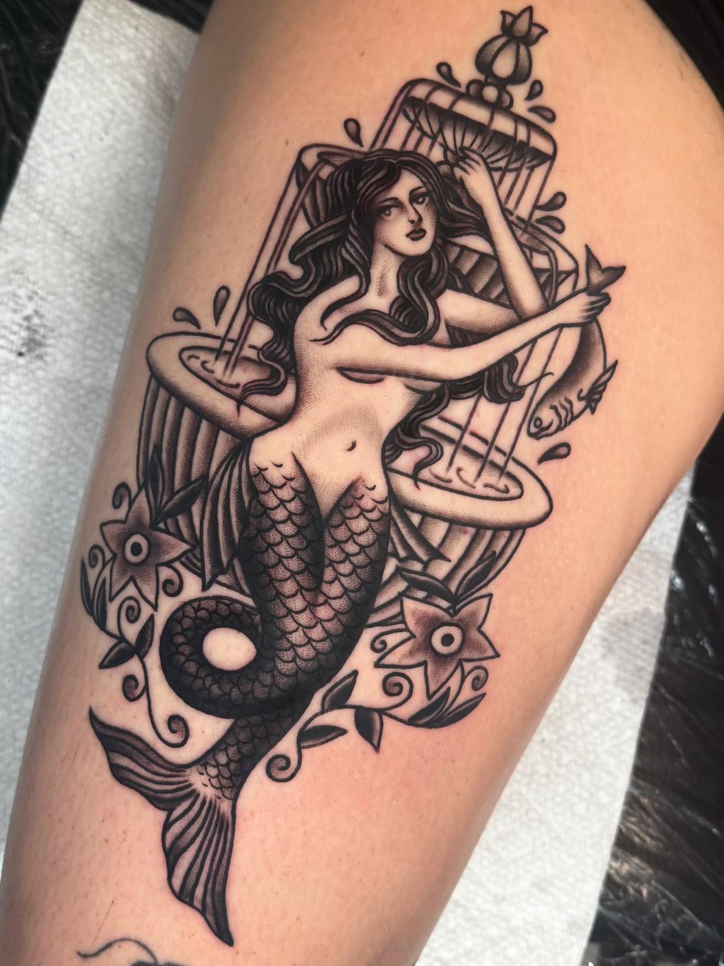 Black and grey mermaid with a birdcage and flowers, on a thigh.