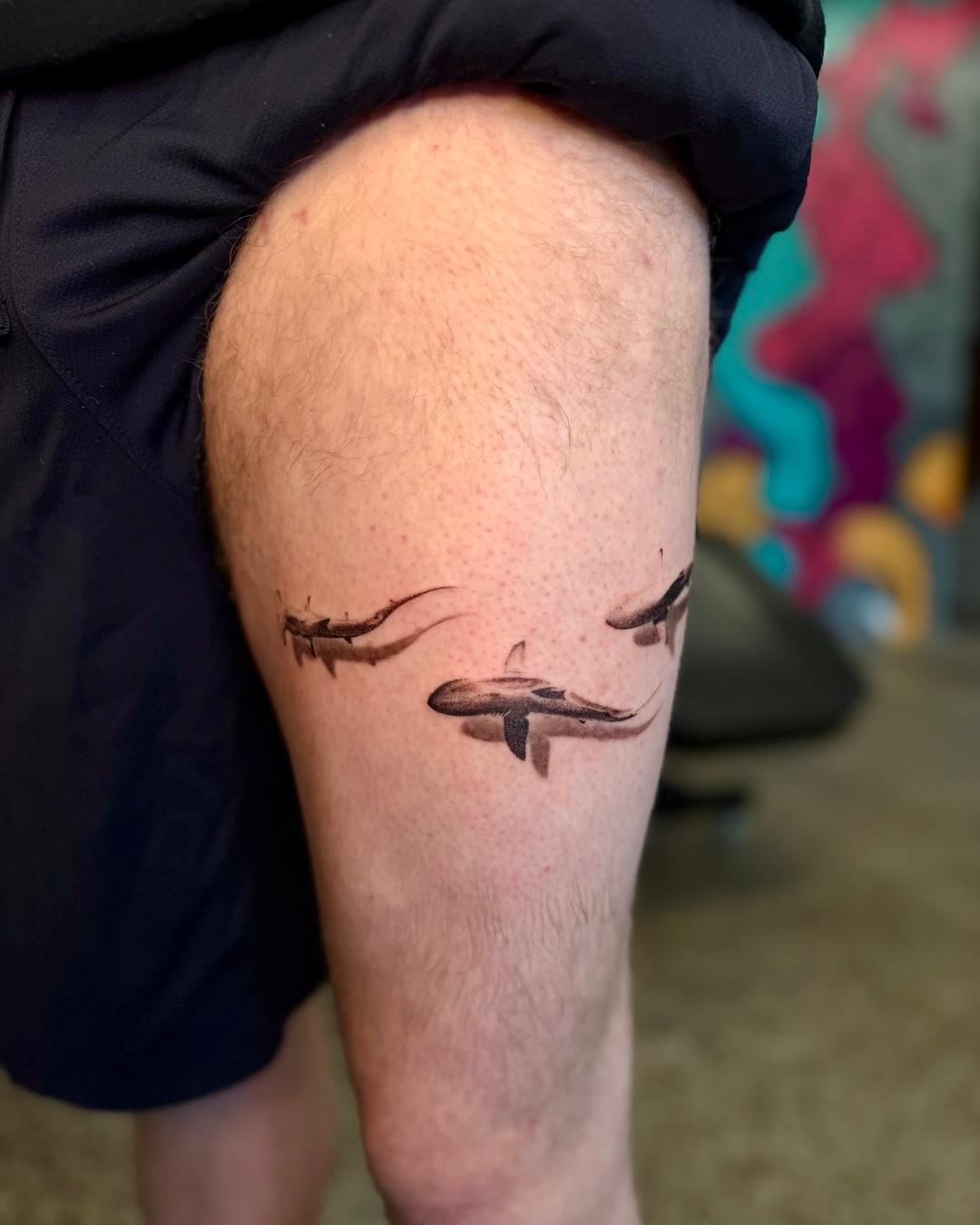 Three fine-line sharks swimming across a thigh.